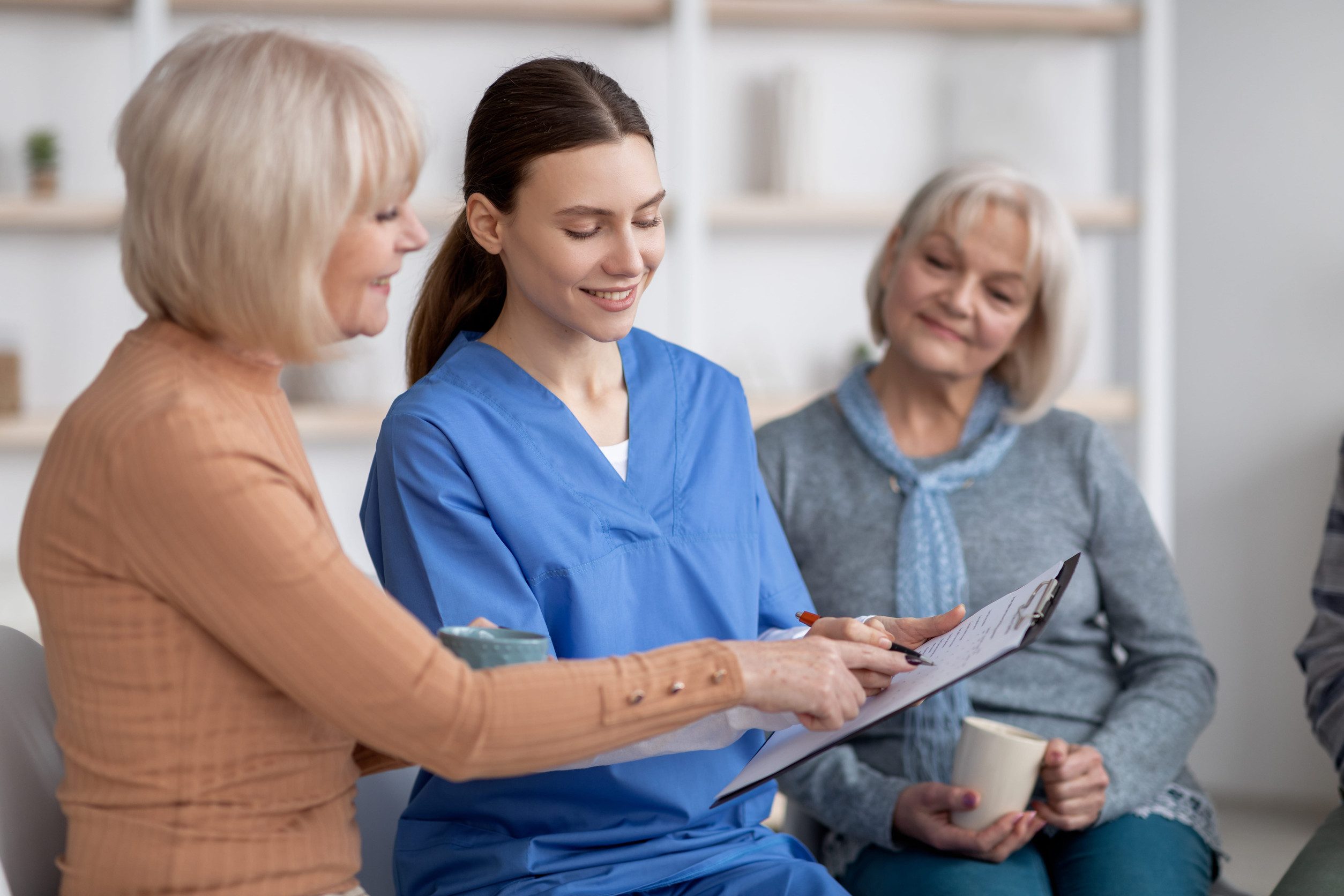 Pretty young nurse questioning senior ladies at nursing home caregiver shortage